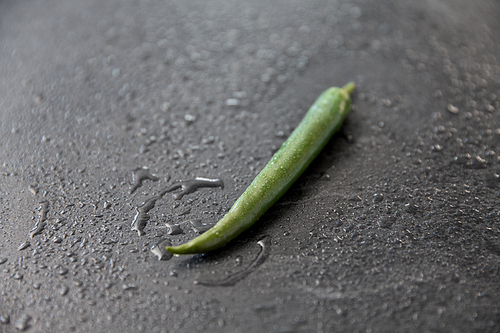 vegetable, food and culinary concept - close up of green chili pepper on slate stone background
