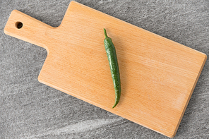 vegetable, food and culinary concept - close up of green chili pepper on wooden cutting board on slate stone background