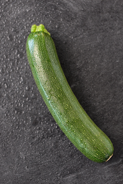 vegetable, food and culinary concept - close up of zucchini on slate stone background