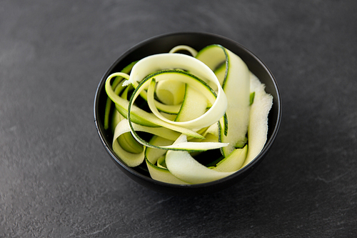 vegetable, food and culinary concept - close up of peeled or sliced zucchini in ceramic bowl on slate stone background