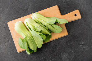 vegetable, food and culinary concept - close up of bok choy chinese cabbage on wooden cutting board on slate stone background