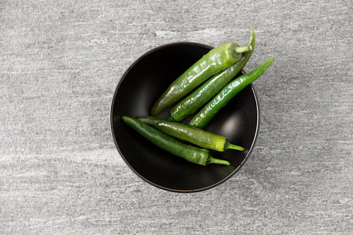 vegetable, food and culinary concept - close up of green chili peppers in ceramic bowl on slate stone background