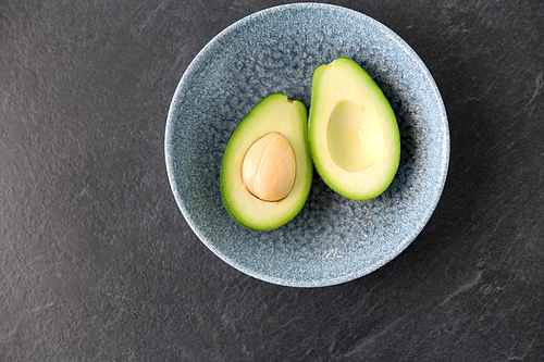 food, eating and vegetable concept - close up of cut avocado with bone in ceramic bowl on slate stone background