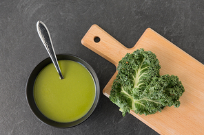 vegetable, food and culinary concept - kale cabbage cream soup in ceramic bowl with spoon on slate stone background