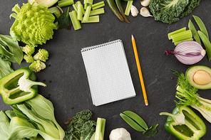 food, diet and healthy eating concept - close up of different green vegetables and diary with empty pages and pencil on slate stone background