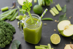 healthy eating, food and vegetarian diet concept - close up of glass mug of fresh green juice or smoothie with paper straw, fruits and vegetables on slate stone background