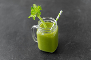 healthy eating, detox and vegetable diet concept - close up of glass mug of green fresh celery juice or smoothie with paper straw on slate stone background