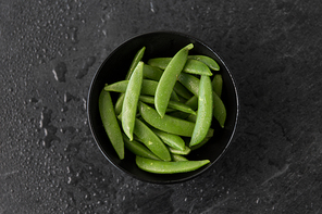 vegetable, food and culinary concept - peas in bowl on wet slate stone background
