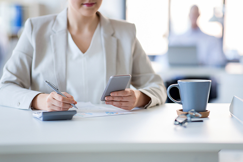 business and people concept - businesswoman with smartphone and papers working at office
