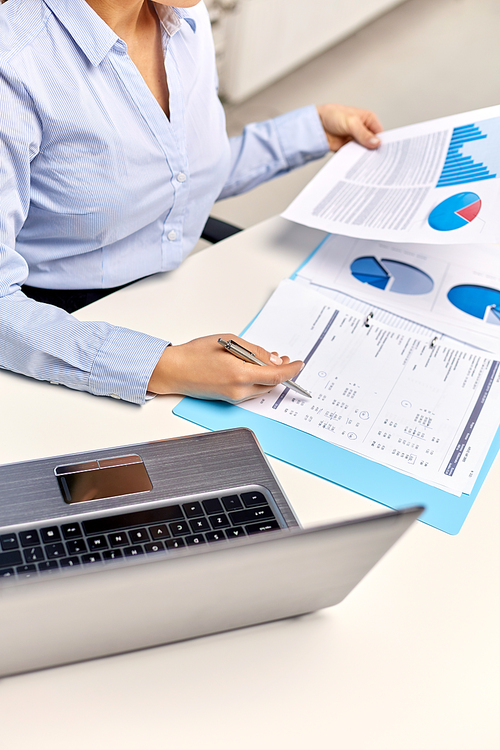 business, deadline and technology concept - businesswoman with papers and laptop computer working at office