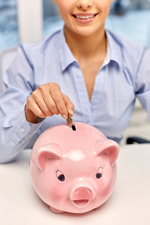 business, finances and investment concept - close up of happy smiling businesswoman with piggy bank and coin at office