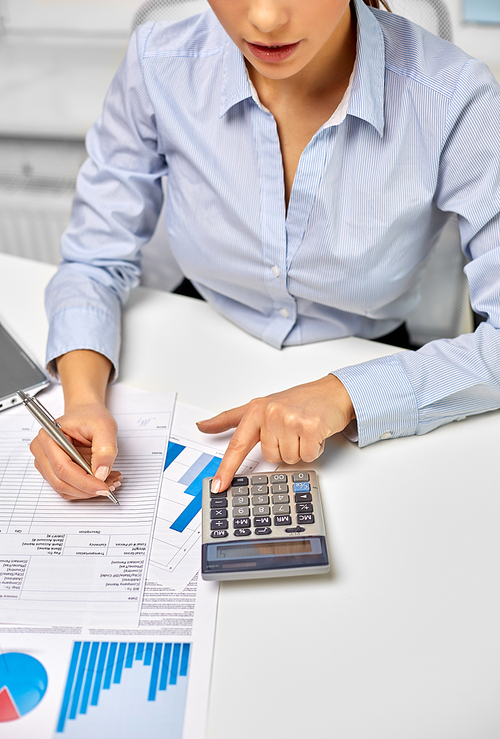 business, finances and accounting concept - close up of businesswoman counting on calculator and filling papers at office