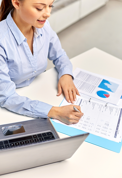 business, deadline and technology concept - businesswoman with papers and laptop computer working at office