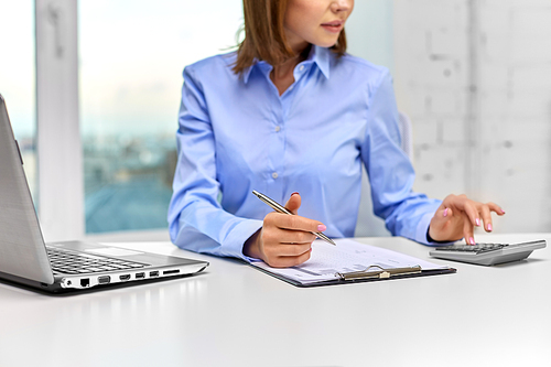 business, finances and accounting concept - close up of businesswoman with laptop computer and calculator filling papers at office