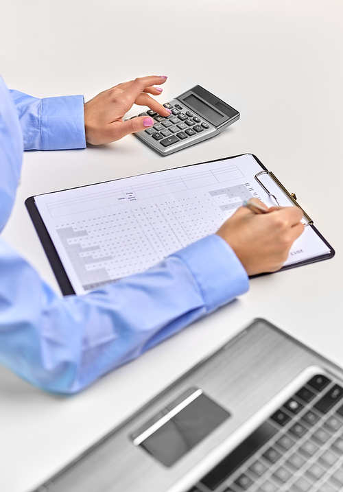 business, finances and accounting concept - close up of businesswoman with laptop computer and calculator filling papers at office