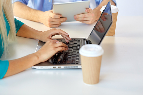 business, break and people concept - close up of woman typing on laptop and coffee cups on table