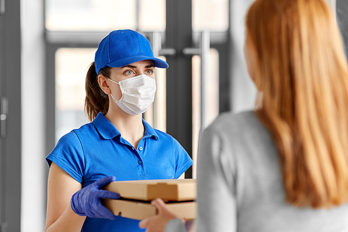 health protection, safety and pandemic concept - delivery woman in medical face mask and gloves giving pizza boxes to female customer at office