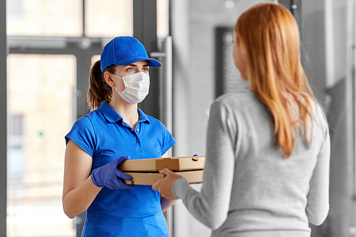 health protection, safety and pandemic concept - delivery woman in medical face mask and gloves giving pizza boxes to female customer at office