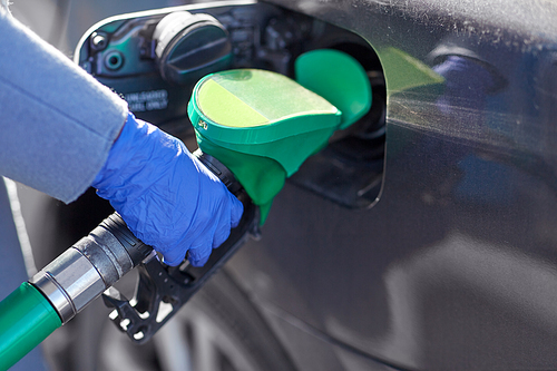 health, safety and pandemic concept - close up of hand in glove filling car with gasoline at gas station
