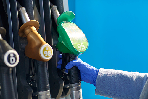 health, safety and pandemic concept - close up of hand in glove gasoline nozzle at gas station