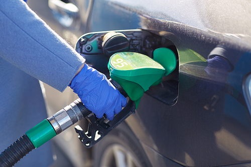 health, safety and pandemic concept - close up of hand in glove filling car with gasoline at gas station