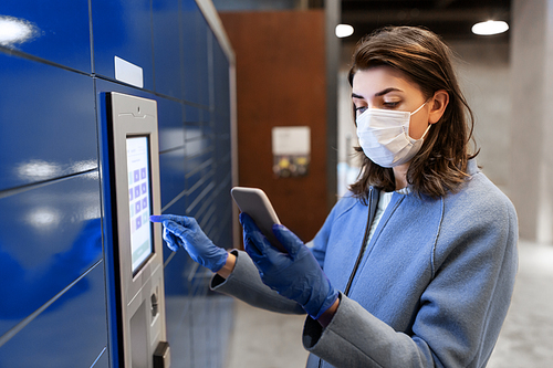 health care, mail delivery and pandemic concept - woman wearing face protective medical mask for protection from virus disease with smartphone entering code on automated parcel machine's touch screen