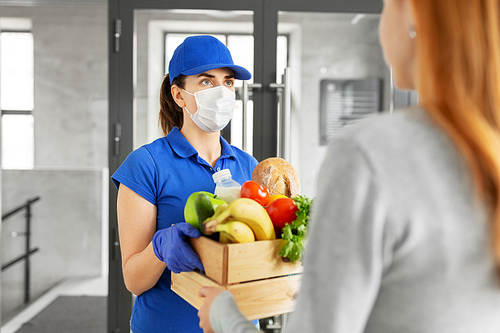 health protection, safety and pandemic concept - delivery woman in protective face mask and gloves giving wooden box with food to female customer at office