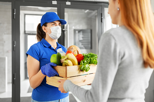 health protection, safety and pandemic concept - delivery woman in protective face mask and gloves giving wooden box with food to female customer at office