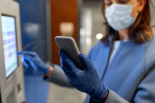 health care,  delivery and pandemic concept - close up of woman wearing medical mask for protection from virus disease with smartphone entering code on automated parcel machine's touch screen