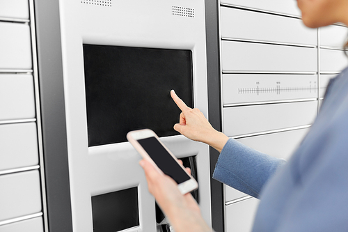 delivery and post service concept - close up of woman with smartphone choosing operation on outdoor automated parcel machine's touch screen