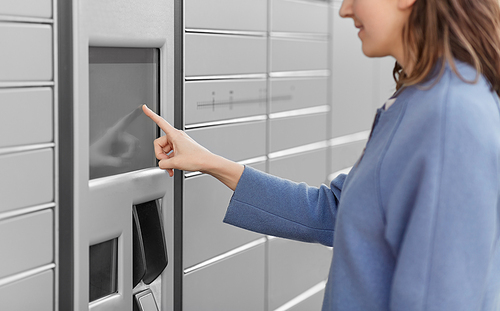 delivery and post service concept - close up of happy smiling woman choosing operation on outdoor automated parcel machine's touch screen