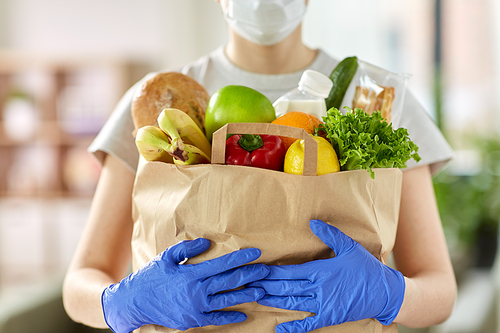 health protection, safety and pandemic concept - close up of woman in protective medical gloves and mask holding food in paper bag at home