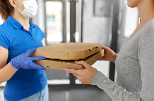 health protection, safety and pandemic concept - delivery woman in medical face mask and gloves giving pizza boxes to female customer at office