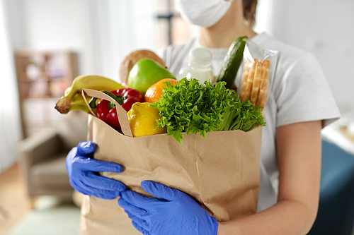 health protection, safety and pandemic concept - close up of woman in protective medical gloves and mask holding food in paper bag at home