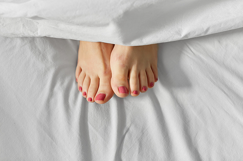 people, bedtime and rest concept - feet of woman lying in bed under white blanket or duvet