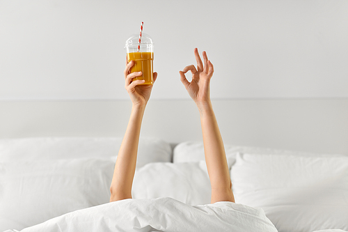 gesture, drink and morning concept - hands of young woman lying in bed with cup of juice showing ok hand sign at bedroom