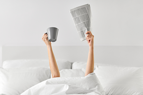morning, news and people concept - young woman with cup of coffee and newspaper lying in bed at home bedroom