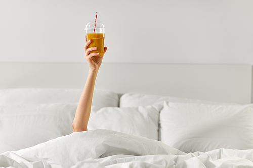 drink, comfort and morning concept - hand of young woman lying in bed with cup of juice at bedroom