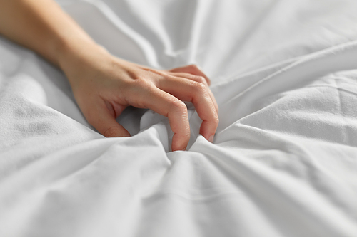 bedtime, sex and rest concept - hand of woman squeezing white bed sheet