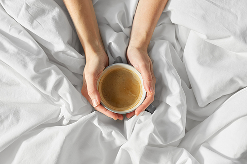 morning, drink and people concept - hands of young woman with cup of coffee in bed at home bedroom