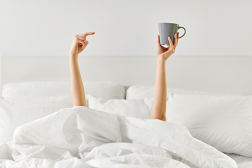 morning, comfort and people concept - young woman with cup of coffee lying in bed at home bedroom