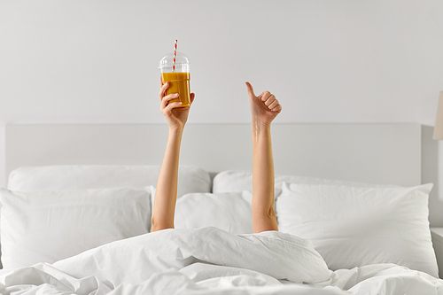 gesture, drink and morning concept - hands of young woman lying in bed with cup of juice showing thumbs up at bedroom