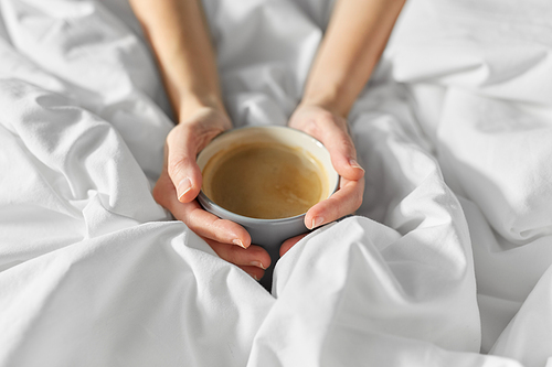 morning, drink and people concept - hands of young woman with cup of coffee in bed at home bedroom
