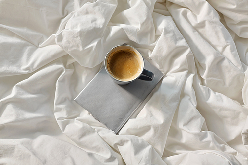 morning, hygge and drink concept - cup of coffee with book in bed at home