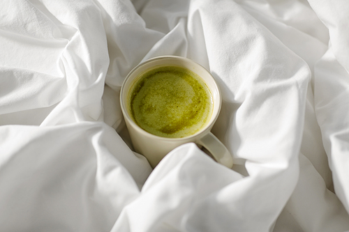 morning, hygge and drink concept - cup of matcha tea in bed at home