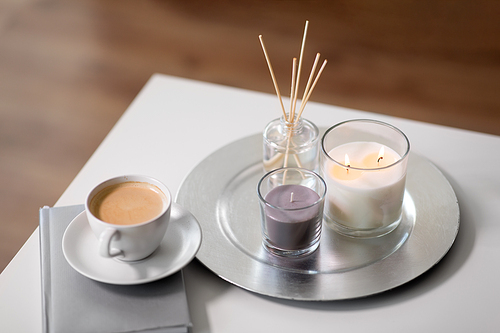 hygge and aromatherapy concept - coffee, candles, book and aroma reed diffuser on table