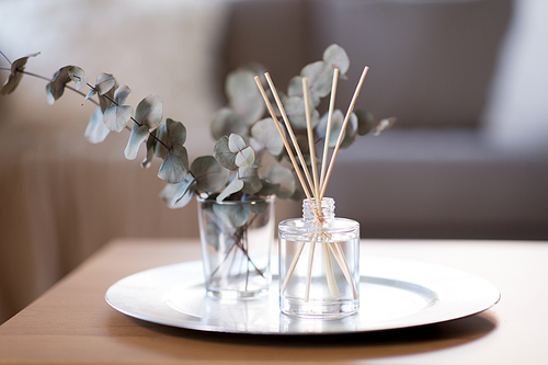 decoration, hygge and aromatherapy concept - aroma reed diffuser and branches of eucalyptus populus on table at home