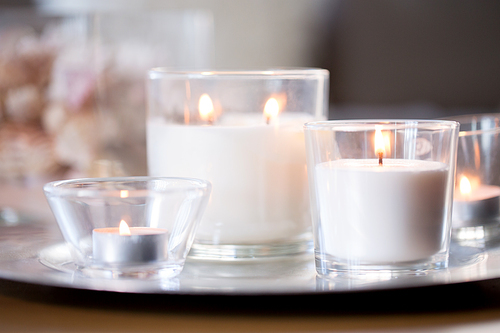 decoration, hygge and cosiness concept - burning white fragrance candles on tray on table