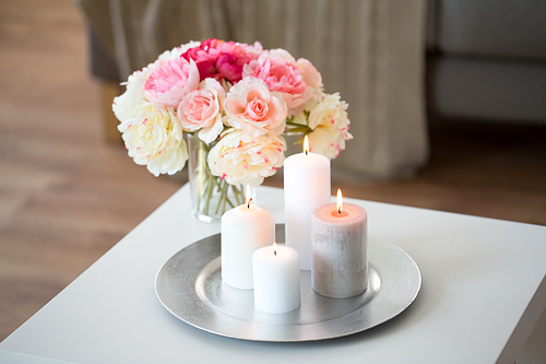 decoration, hygge and cosiness concept - candles burning on table and flowers at cozy home