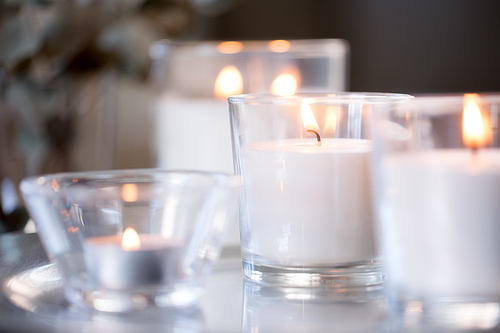 decoration, hygge and cosiness concept - burning white fragrance candles on table